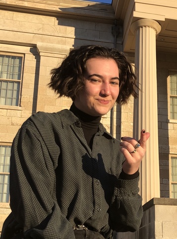 A person with brown hair sitting in front of the Iowa Old Capitol building.